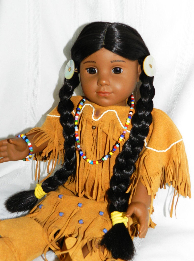 May include: A Native American doll with long black braids, wearing a brown suede dress with fringe and beaded jewelry. The doll has brown eyes and dark skin.