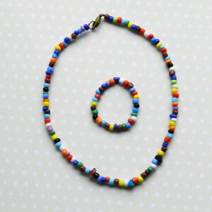 May include: A colorful beaded necklace and bracelet set. The necklace is long and features a variety of colors, including red, blue, green, yellow, and white. The bracelet is shorter and features the same colors as the necklace.