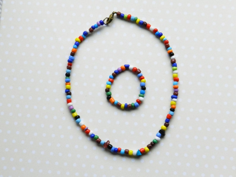May include: A colorful beaded necklace and bracelet set. The necklace is long and features a variety of colors, including red, blue, green, yellow, and white. The bracelet is shorter and features the same colors as the necklace.