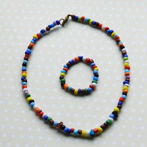 May include: A colorful beaded necklace and bracelet set. The necklace is long and features a variety of colors, including red, blue, green, yellow, and white. The bracelet is smaller and features the same colors as the necklace.