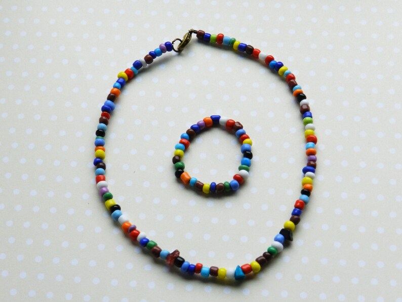 May include: A colorful beaded necklace and bracelet set. The necklace is long and features a variety of colors, including red, blue, green, yellow, and white. The bracelet is smaller and features the same colors as the necklace.