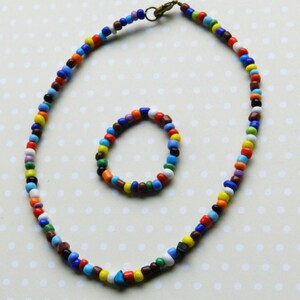 May include: A colorful beaded necklace and bracelet set. The necklace is long and has a variety of colors, including red, orange, yellow, green, blue, purple, and brown. The bracelet is shorter and has the same colors as the necklace.