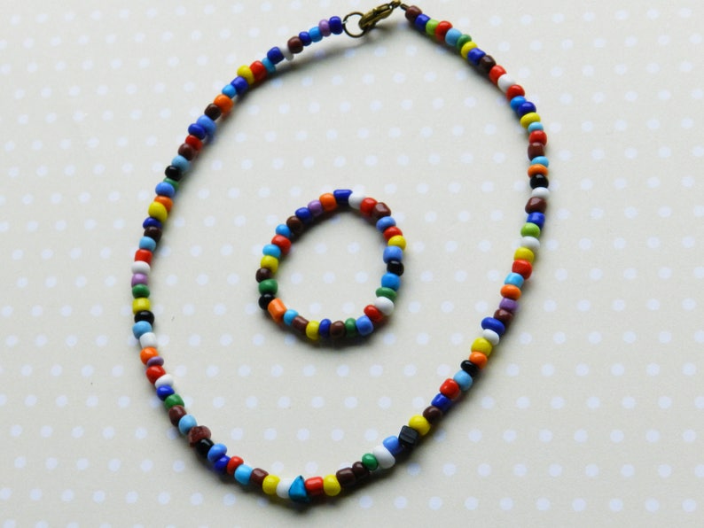May include: A colorful beaded necklace and bracelet set. The necklace is long and has a variety of colors, including red, orange, yellow, green, blue, purple, and brown. The bracelet is shorter and has the same colors as the necklace.