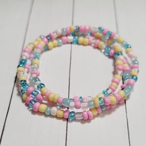 May include: A multi-strand beaded bracelet with pink, yellow, and blue beads. The bracelet is made of small, round beads and is wrapped around itself several times.