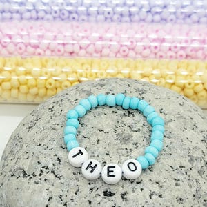May include: A light blue beaded bracelet with the name "THEO" spelled out in white beads.