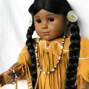 May include: A doll with long black braids wearing a brown suede dress with fringe and a colorful beaded necklace. The doll has brown eyes and dark skin.