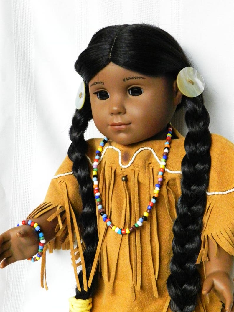 May include: A doll with long black braids wearing a brown suede dress with fringe and a colorful beaded necklace. The doll has brown eyes and dark skin.