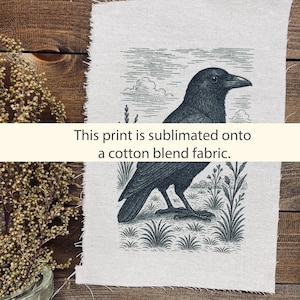 May include: A black crow illustration printed on a cotton blend fabric. The crow is depicted in a detailed, vintage style, with a grassy foreground and cloudy sky background. The text "This print is sublimated onto a cotton blend fabric" is also visible.