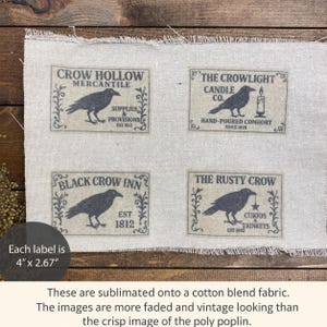 May include: A rectangular piece of light beige cotton blend fabric featuring four printed labels, each measuring 4 inches by 2.67 inches. The labels display black illustrations of crows with text including Crow Hollow Mercantile, The Crowlight Candle Co., Black Crow Inn, and The Rusty Crow, all framed by decorative scrollwork.