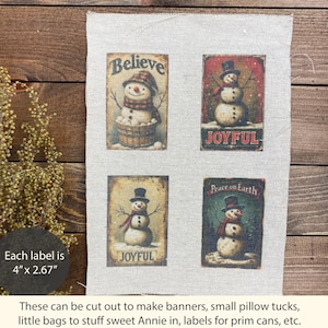 May include: A rectangular piece of light beige fabric featuring four printed rectangular labels with snowman illustrations. Each label measures 4 inches by 2.67 inches. The designs include snowmen with hats and scarves, and text reading Believe, Joyful, and Peace on Earth.