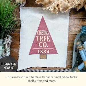 May include: A rectangular off-white fabric panel measuring 9 inches by 5.5 inches, featuring a maroon triangular Christmas tree graphic with the text CHRISTMAS TREE CO. and 1884 printed in cream, with a small brown rectangular trunk.