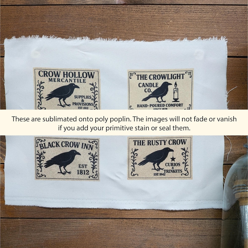 May include: A white poly poplin fabric sheet featuring four rectangular labels with black crow illustrations and text: Crow Hollow Mercantile, The Crowlight Candle Co., Black Crow Inn, and The Rusty Crow, with frayed edges on the top and bottom.
