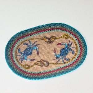 May include: Oval-shaped woven rug with a blue and white crab design on a beige background. The rug has a turquoise border with red, green, and brown accents.