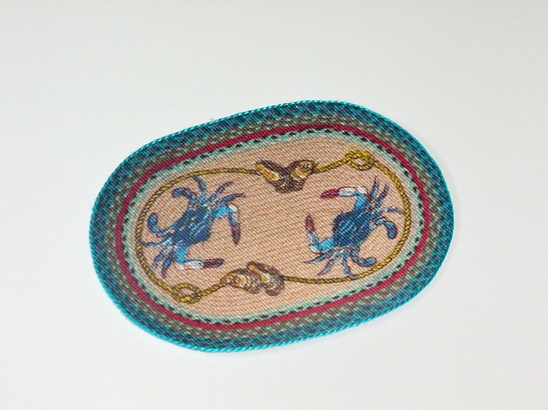 May include: Oval-shaped woven rug with a blue and white crab design on a beige background. The rug has a turquoise border with red, green, and brown accents.