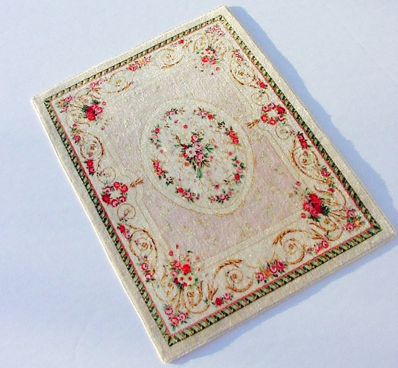 May include: A white and pink floral patterned rug with a gold and green border. The rug has a central oval design with a floral pattern.