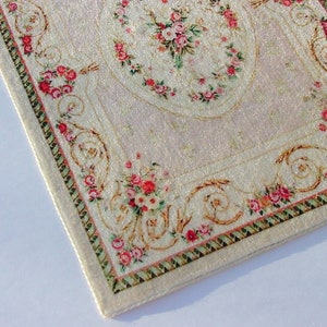 May include: A white rug with a pink and green floral pattern. The rug has a gold border with a repeating design.