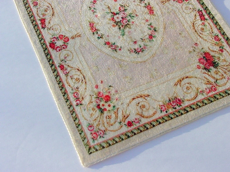 May include: A white rug with a pink and green floral pattern. The rug has a gold border with a repeating design.