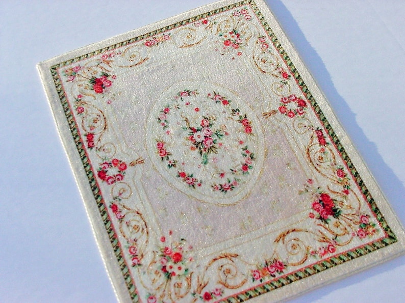 May include: A white rug with a floral pattern in shades of pink and green. The rug has a border with a gold and green design.