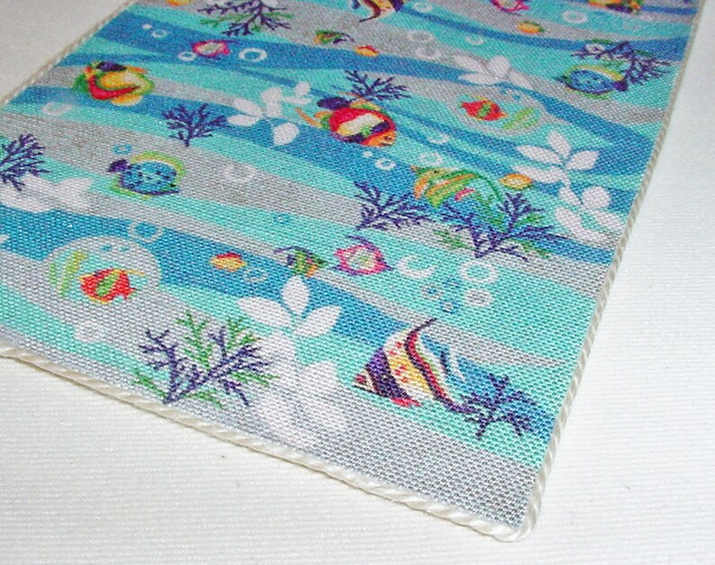 May include: A blue and white fabric with a repeating pattern of colourful fish, seaweed, and bubbles. The fabric has a white border.