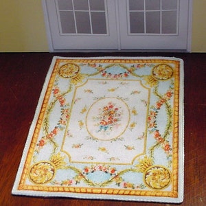May include: A white and blue floral patterned rug with a yellow border. The rug has a central oval design with a bouquet of flowers. The rug is approximately 12 inches by 16 inches.