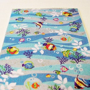 May include: A blue and grey fabric with a repeating pattern of colourful fish, seaweed, and bubbles. The fabric has a white border.