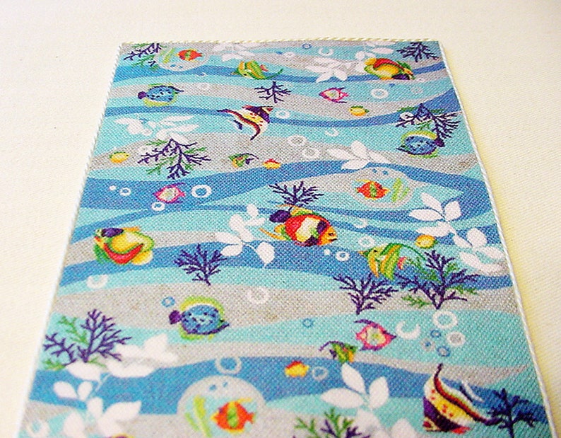 May include: A blue and grey fabric with a repeating pattern of colourful fish, seaweed, and bubbles. The fabric has a white border.