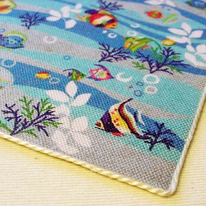 May include: A blue and grey fabric with a white border. The fabric features a repeating pattern of colourful fish, seaweed, and bubbles.