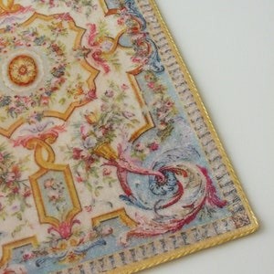 May include: A vintage-style rug with a floral and scroll design in shades of pink, blue, yellow, and green. The rug has a gold border with a repeating pattern.
