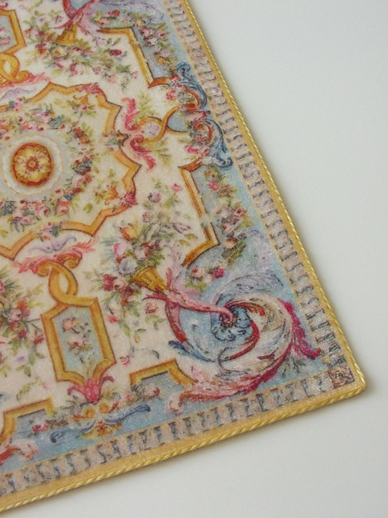 May include: A vintage-style rug with a floral and scroll design in shades of pink, blue, yellow, and green. The rug has a gold border with a repeating pattern.