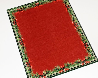 May include: Red Christmas-themed rug with a green and white plaid border and a green garland with red berries and bows.