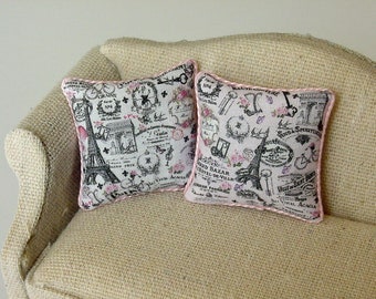 May include: Two decorative throw pillows with a pink trim and a white background. The pillows feature a black and white print of the Eiffel Tower and other Parisian imagery. The pillows are on a beige couch.