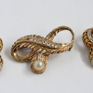 May include: Three gold-tone brooches with a leaf design and clear rhinestones. The center brooch features a faux pearl.