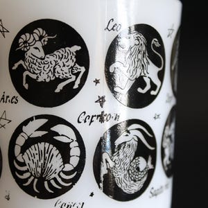 May include: White cylindrical object with black zodiac symbols, including Aries, Leo, and Capricorn. Each symbol is in a black circle with the zodiac name below. The object has a glossy finish.