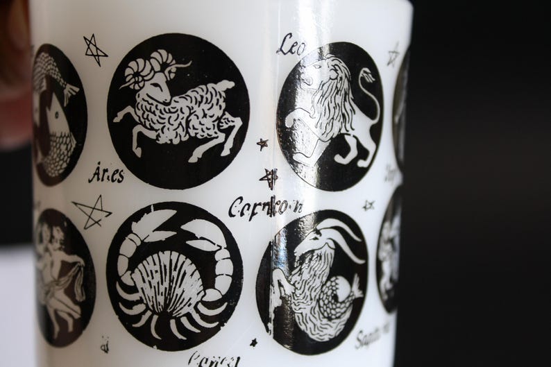 May include: White cylindrical object with black zodiac symbols, including Aries, Leo, and Capricorn. Each symbol is in a black circle with the zodiac name below. The object has a glossy finish.