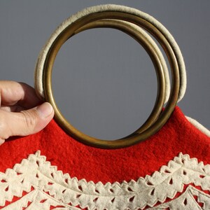 Puede incluir: Bolso de fieltro rojo con ribete de crochet blanco y asa de doble anillo de lat&oacute;n.