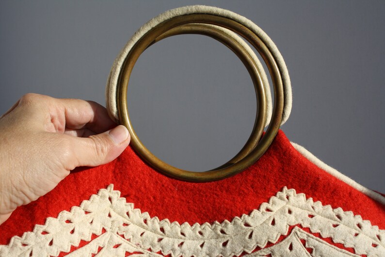 Puede incluir: Bolso de fieltro rojo con ribete de crochet blanco y asa de doble anillo de lat&oacute;n.