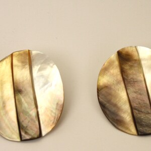 May include: A pair of round, iridescent earrings made from mother of pearl. The earrings have a light brown and white color with a striped pattern.