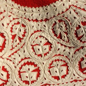 Puede incluir: Primer plano de una tela roja con dise&ntilde;os florales bordados en blanco. El bordado es intrincado y detallado, creando un patr&oacute;n hermoso.