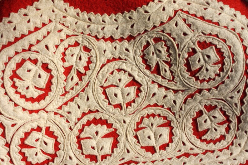 Puede incluir: Primer plano de una tela roja con dise&ntilde;os florales bordados en blanco. El bordado es intrincado y detallado, creando un patr&oacute;n hermoso.