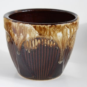 May include: A brown and white glazed ceramic planter with a drip glaze design. The planter has a wide, round opening and a slightly flared lip.