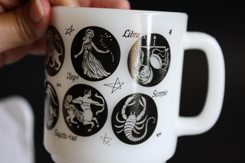May include: White ceramic mug featuring black zodiac symbols and star accents. The mug includes the signs Virgo, Libra, Scorpio, and Sagittarius. The mug has a white handle and a classic design.