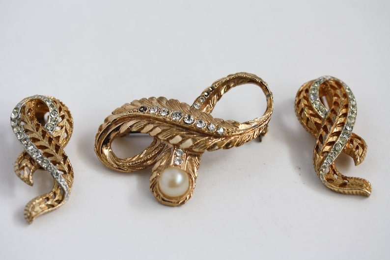 May include: Three gold-tone brooches with a leaf design and clear rhinestones. The center brooch features a faux pearl.