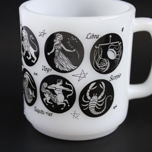 May include: White ceramic mug featuring black zodiac symbols and names. The mug has a rounded body and a large handle. Zodiac signs include Virgo, Libra, and Scorpio. A unique gift for astrology enthusiasts.