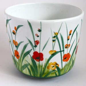 Peut inclure: Pot en céramique blanche avec un motif floral vert, orange et rouge. Le pot a une forme arrondie et une large ouverture.