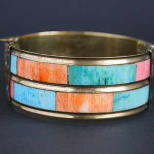 May include: A brass bangle bracelet with two rows of inlaid turquoise and coral stones. The bracelet has a hinged clasp.