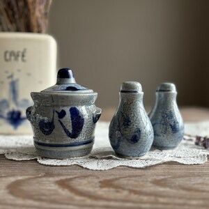 May include: A set of three blue and white ceramic salt and pepper shakers with a textured finish. The shakers have a traditional design with blue floral patterns.