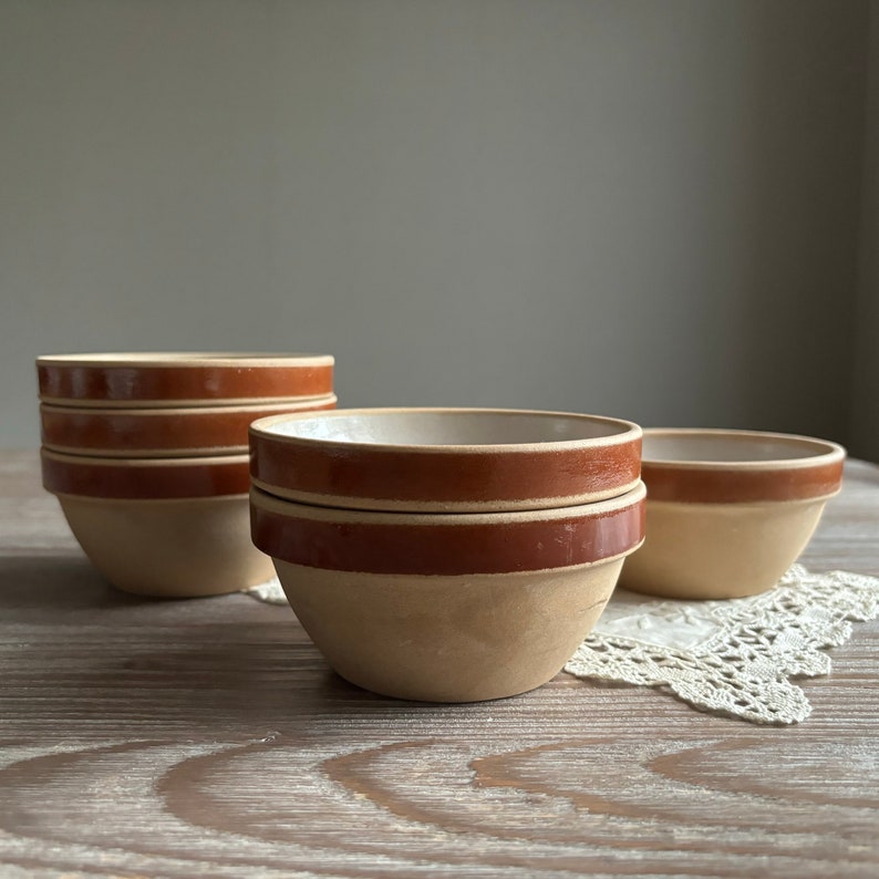 May include: A set of four brown and beige ceramic bowls with a brown rim. The bowls are stacked on a wooden surface.