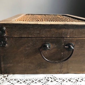 Puede incluir: Una caja de madera con una tapa tejida y una manija de metal. La caja es marr&oacute;n y tiene detalles met&aacute;licos.