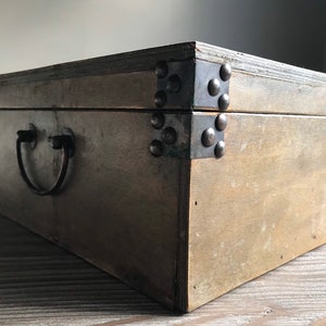 Puede incluir: Una caja de madera con una manija y bisagras de metal. La caja tiene un acabado marr&oacute;n oscuro y est&aacute; decorada con tachuelas de metal.