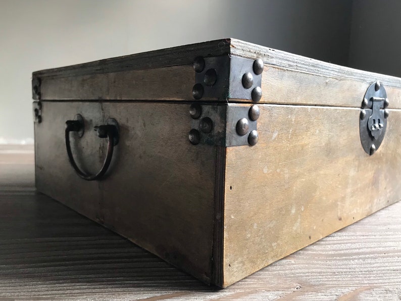 Puede incluir: Una caja de madera con una manija y bisagras de metal. La caja tiene un acabado marr&oacute;n oscuro y est&aacute; decorada con tachuelas de metal.